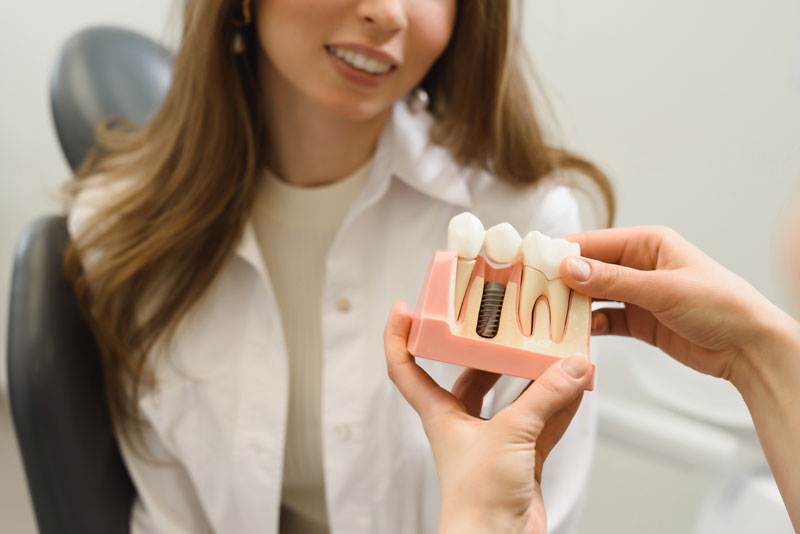 An image of a dentist holding a dental implant model to show a dental patient.